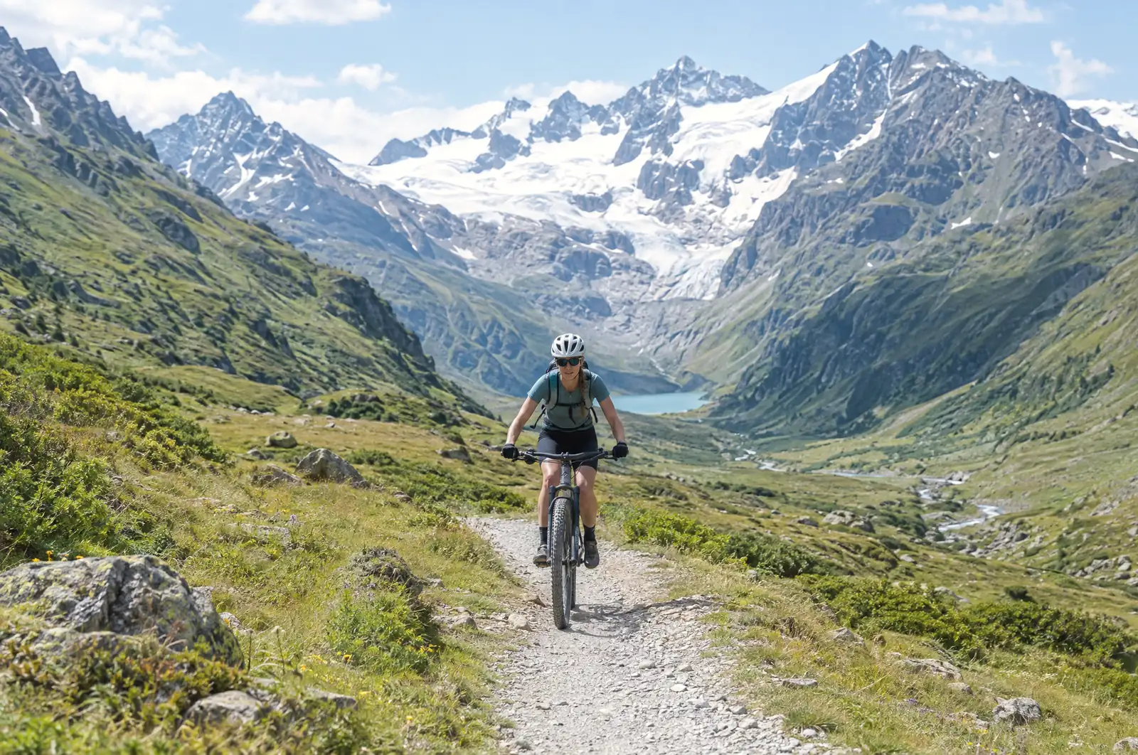 Cyclist on a gravel track through a high alpine valley, a glacier in the background