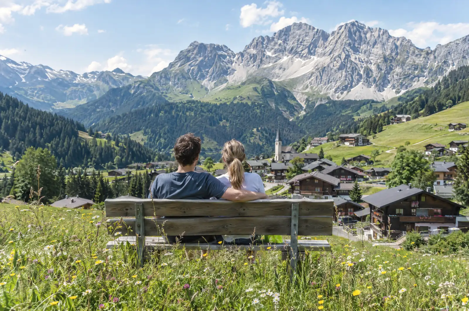 Couple on a bench in a flower meadow above a mountain village with wooden houses